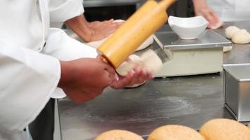 Close up of chefs' hand in white cook uniforms and aprons are kneading raw pastry dough, preparing bread, cakes, cakes, and fresh bakery food, baking in oven at stainless steel kitchen of restaurant.
