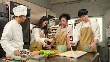 curso de culinária, um chef masculino sênior em uniforme de cozinheiro ensina jovens alunos de aulas de culinária a preparar ingredientes e massa de pastelaria para alimentos de padaria e tortas de frutas em uma cozinha de aço inoxidável de restaurante. video