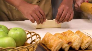 close-up na mão do chef em uniforme de cozinheiro com avental, alunos de aula de culinária rolam e enchem ingredientes em massa de pastelaria para alimentos de padaria, preparam tortas de frutas na cozinha de aço inoxidável do restaurante. video