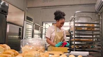 entrega de pequenas empresas de inicialização de padaria. uma cozinheira afro-americana está embalando pães e doces feitos à mão e recém-assados em caixas e enviando para compras on-line de clientes na cozinha culinária. video