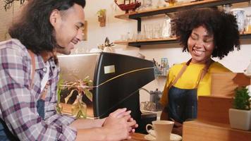Two cafe business startup partners and friends, African American female, and Thai male baristas talk and cheerful smile together at counter bar of coffee shop, happy service job, and SME entrepreneur. video