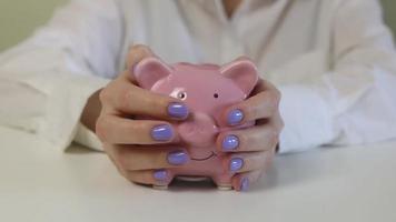 Close-up of women's hands, stroking a pink piggy bank on a wooden table. video