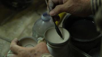 Female hand holding a paint brush to paint clay products, close-up. The process of hand-painting a ceramic hand-made bowl.