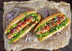 Homemade hot dog with sausage, salad, carrot, cucumber and tomato on wooden background photo