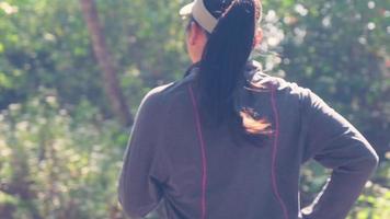 asiatische frau, die auf unbefestigter straße im wald joggt, um zu trainieren. sportliche Frau, die morgens auf einer Landstraße unter grünen Bäumen läuft. video
