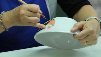 Female hand holding a paint brush to paint clay products, close-up. The process of hand-painting a ceramic hand-made bowl. video