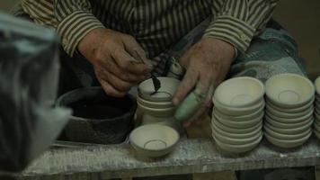 mano femenina sosteniendo un pincel para pintar productos de arcilla, primer plano. el proceso de pintar a mano un cuenco de cerámica hecho a mano. video