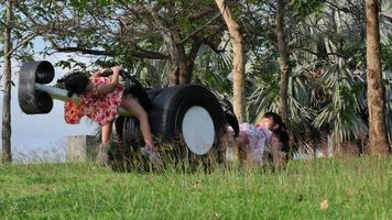 lindos niños jugando en el patio de recreo al aire libre. las hermanas pequeñas se sientan en una sierra de balancín hecha de neumáticos viejos en el parque. Actividad de verano saludable para niños. video