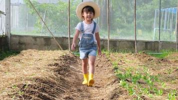 una niña con sombrero ayuda a su madre en el jardín, una pequeña jardinera. linda chica jugando en el huerto. video