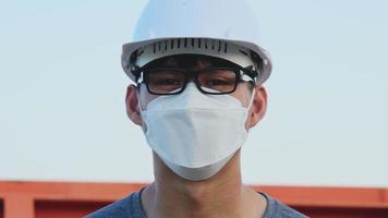 Young Asian engineer wearing a helmet and mask looks and smiles video