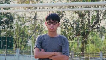 Portrait of a confident young man wearing glasses and wearing a gray t-shirt standing in front of a soccer goal in a summer park video