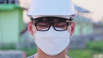 Young Asian engineer wearing a helmet and mask looks and smiles video