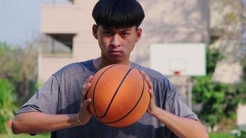 jeune athlète asiatique portant des écouteurs pose avec un basket-ball sur un terrain extérieur video