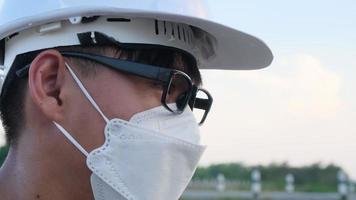 Young Asian engineer wearing a helmet and mask looks. video