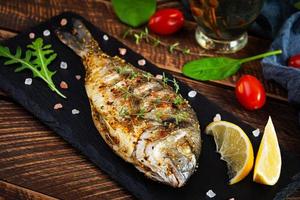 Grilled dorado fish on wooden background. Roasted seafish with spice and herbs photo