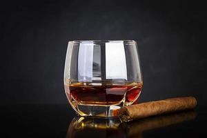 vaso de whisky y cigarro sobre fondo oscuro.