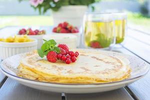 Pancakes with caramelized apples, raspberries, strawberries and red currants. Brunch with green tea and crepes. photo