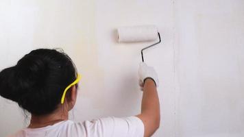 Young woman decorator wearing protective goggles paints the walls with a roller. Repair and interior decoration. video