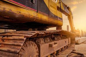 Closeup dirt track pad of backhoe. Digger parked at construction site. Bulldozer near concrete pole. Earth moving machine. Yellow digger with bucket. Earth moving machine. Excavation vehicle. photo