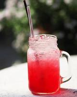 bebida con sabor a agua de soda de limón rojo, bebidas frías con hielo en vidrio transparente con pajitas de papel y plástico sobre mesa blanca foto