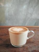 café con leche caliente en vidrio con arte de café con leche en forma de corazón sobre una mesa de madera vieja marrón en concepto de cafetería, comida y bebida. foto