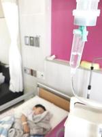 Focus on saline set with blurred background of asian boy sleeping  on hospital bed. Medical equipment concept photo