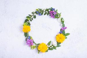 Summer or spring composition on grey background. Purple and yellow flowers, and green leaves with copy space wreath top view. Summer, spring floral concept photo