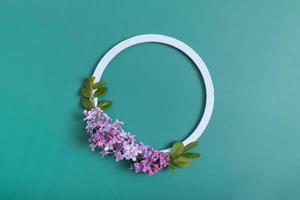 Summer or spring composition on a green background. Lilac flowers with round wooden frame copy space top view. Summer, spring floral concept photo