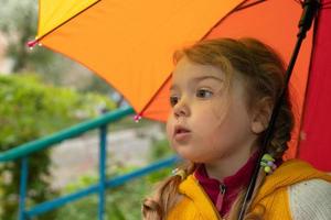 A 3-year-old girl hides in the rain under a colored umbrella photo