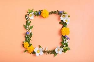 Summer or spring composition on a orangr background. Square frame from flowers and leaves with a copy space top view. Summer, spring floral concept photo