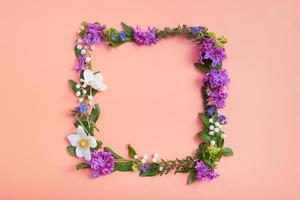 Summer or spring composition on orangr background. Purple flowers, anemone and green leaves with copy space wreath top view. Summer, spring floral concept photo