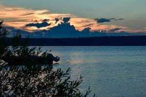 Silhouette of a boat behind leaves in sunset over a lake photo