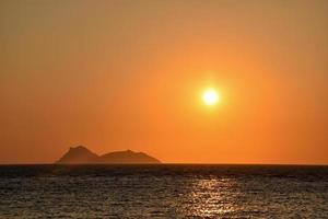 Orange sunset on Matala hippy beach with view on Paximadia islands in Crete, Greece photo