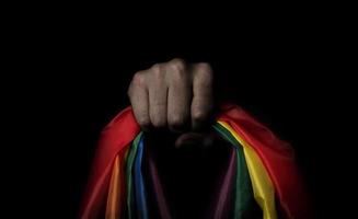 LGBTQ pride flag on black background. Lgbt rainbow flag in gay hand. photo