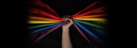 LGBTQ pride flag on black background. Lgbt rainbow flag in gay hand. photo