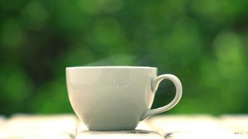 white ceramic coffee mug On the wooden floor, green tree bokeh background. soft focus.shallow focus effect. video