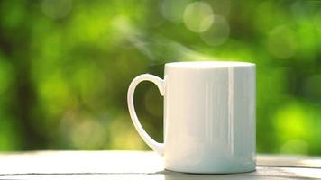 conceito de bebida de café quente, close-up fumegante café quente, xícara de café branco de cerâmica quente com fumaça em uma velha mesa de madeira em um fundo natural. video