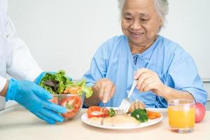 Asian senior or elderly old lady woman patient eating Salmon steak breakfast with vegetable healthy food while sitting and hungry on bed in hospital. photo