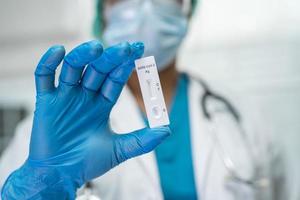 médico asiático en traje de ppe muestra un resultado positivo de la prueba con el kit de prueba de antígeno de saliva para verificar el coronavirus covid-19 en el hospital. foto