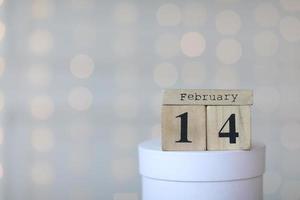 Valentine's day concept. Date 14 February on wooden red cube calendar on a white gift box. Bokeh golden and white background. photo