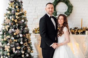 Young couple in love bride and groom posing in studio on background decorated with Christmas tree in their wedding day at Christmas. Enjoy a moment of happiness and love. photo