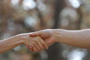 apretón de manos a dos personas en el fondo de la naturaleza. primer plano de mujeres y hombres cogidos de la mano. tomarse de la mano es una forma de intimidad física que involucra a dos o más personas. puede o no ser romántico. foto