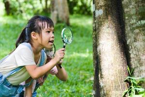 Children learn and explore nature with an outdoor magnifying glass. Curious child looks through a magnifying glass at the trees in the park.  Two little sisters playing with magnifying glass. photo