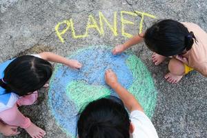 Volunteer family paints a beautiful world with the message Planet on asphalt. Little children and young woman drawing with colorful chalk on courtyard. Concept of world environment day. photo