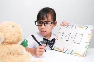 Cute Asian little girl playing teacher role game. A little girl is teaching math to her teddy bear friend. Homeschool children's play and learning. photo
