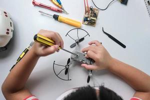 Concentrated little girl repairing her toy drone with a tool in hand and carefully assembles toy drone with screwdriver. STEM Hobbies for advanced smart kids. photo