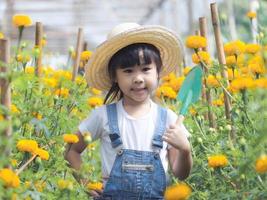 Cute little girl in hat holding garden tool shovel for planting flowers in the garden. A child helps mom in the garden, a little gardener.