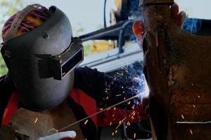 Skilled metalworkers wearing welding masks and gloves work in the home workshop with an arc welding machine. Worker welding metal with sparks, close-up photo
