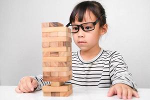 Asian children playing wooden blocks on table at home. Cute little girl having fun playing with building blocks. Wooden block tower building game. Toys for the development of children photo
