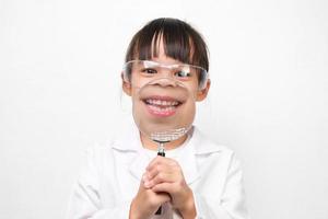 retrato de un pequeño científico sonriente sosteniendo una lupa sobre un fondo blanco. un papel de niña jugando con un disfraz de médico o científico. foto